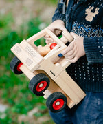 Classic wooden unimog truck by Fagus with peg dolls, carried by child outside.