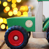 Wooden toy truck with red wheels on a wooden surface, blurred lights in the background