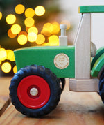 Wooden toy truck with red wheels on a wooden surface, blurred lights in the background