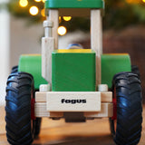 Wooden toy tractor with 'fagus' branding on a wooden surface with blurred lights in the background