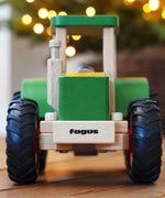 Wooden toy tractor with 'fagus' branding on a wooden surface with blurred lights in the background
