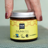 Hand holding a glass pot of Fairtrade Shea Body Butter by Fair Squared, vegan and cruelty free, sold at Babipur.