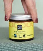 Hand holding a glass pot of Fairtrade Shea Body Butter by Fair Squared, vegan and cruelty free, sold at Babipur.
