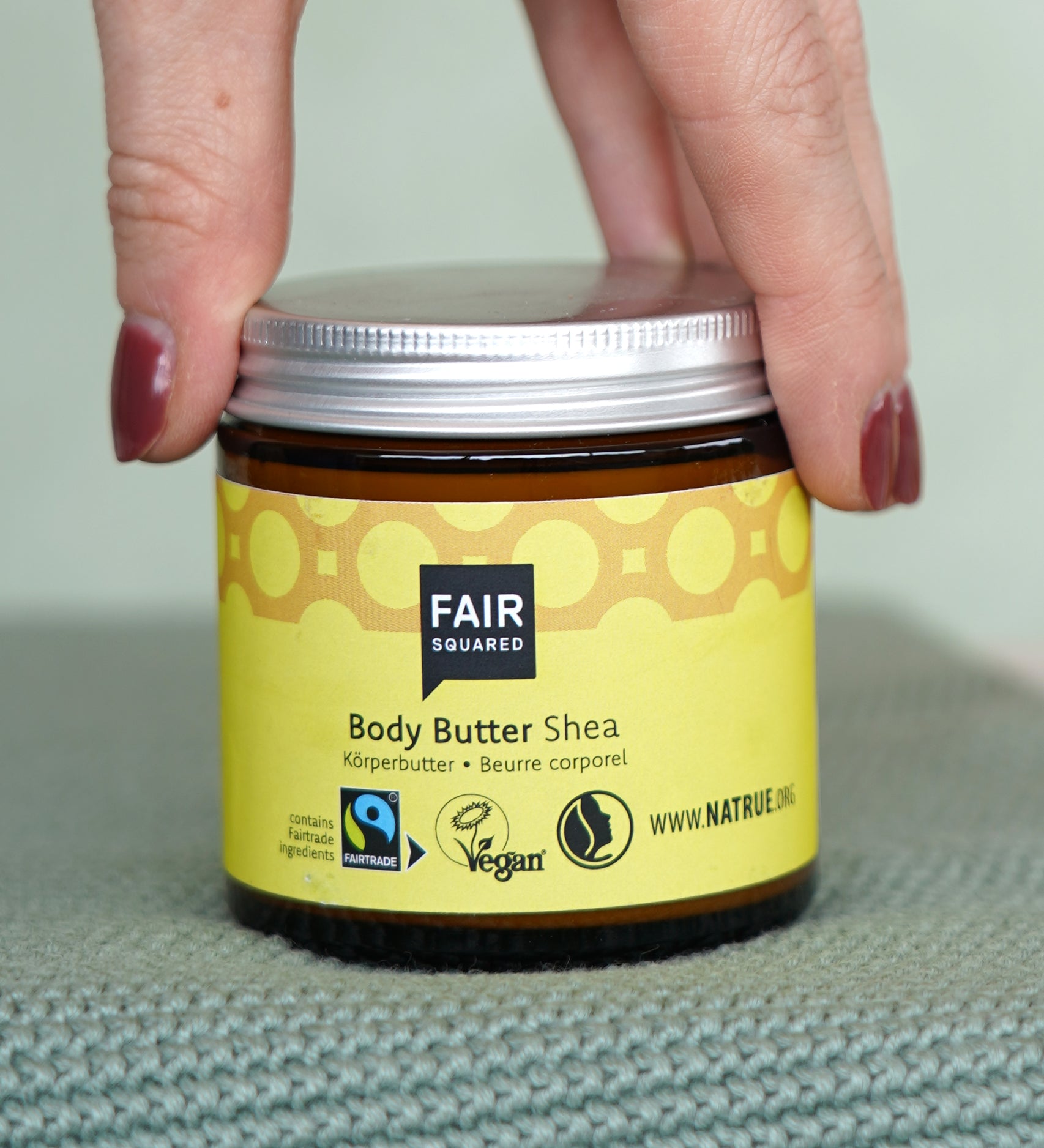 Hand holding a glass pot of Fairtrade Shea Body Butter by Fair Squared, vegan and cruelty free, sold at Babipur.