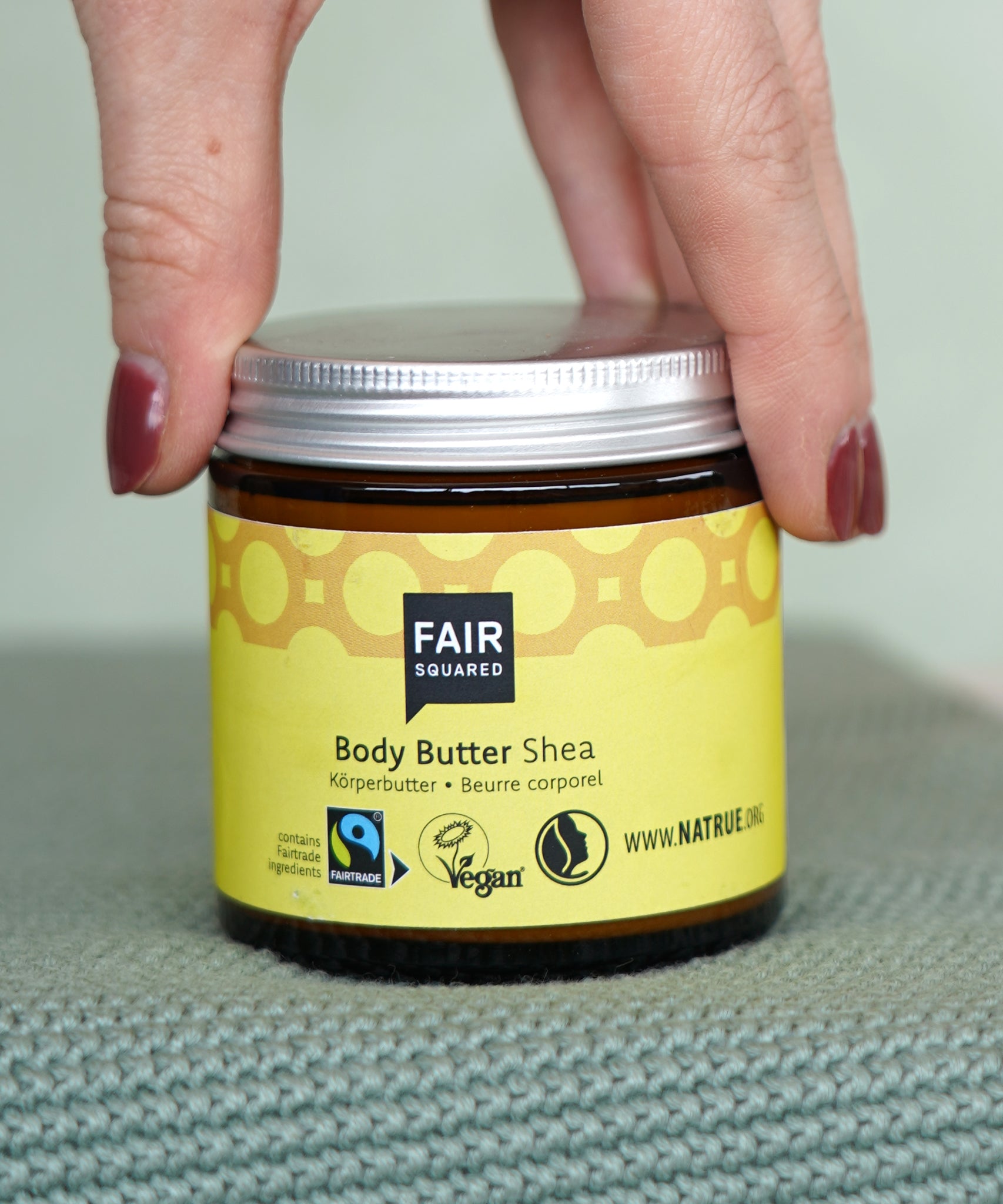 Hand holding a glass pot of Fairtrade Shea Body Butter by Fair Squared, vegan and cruelty free, sold at Babipur.