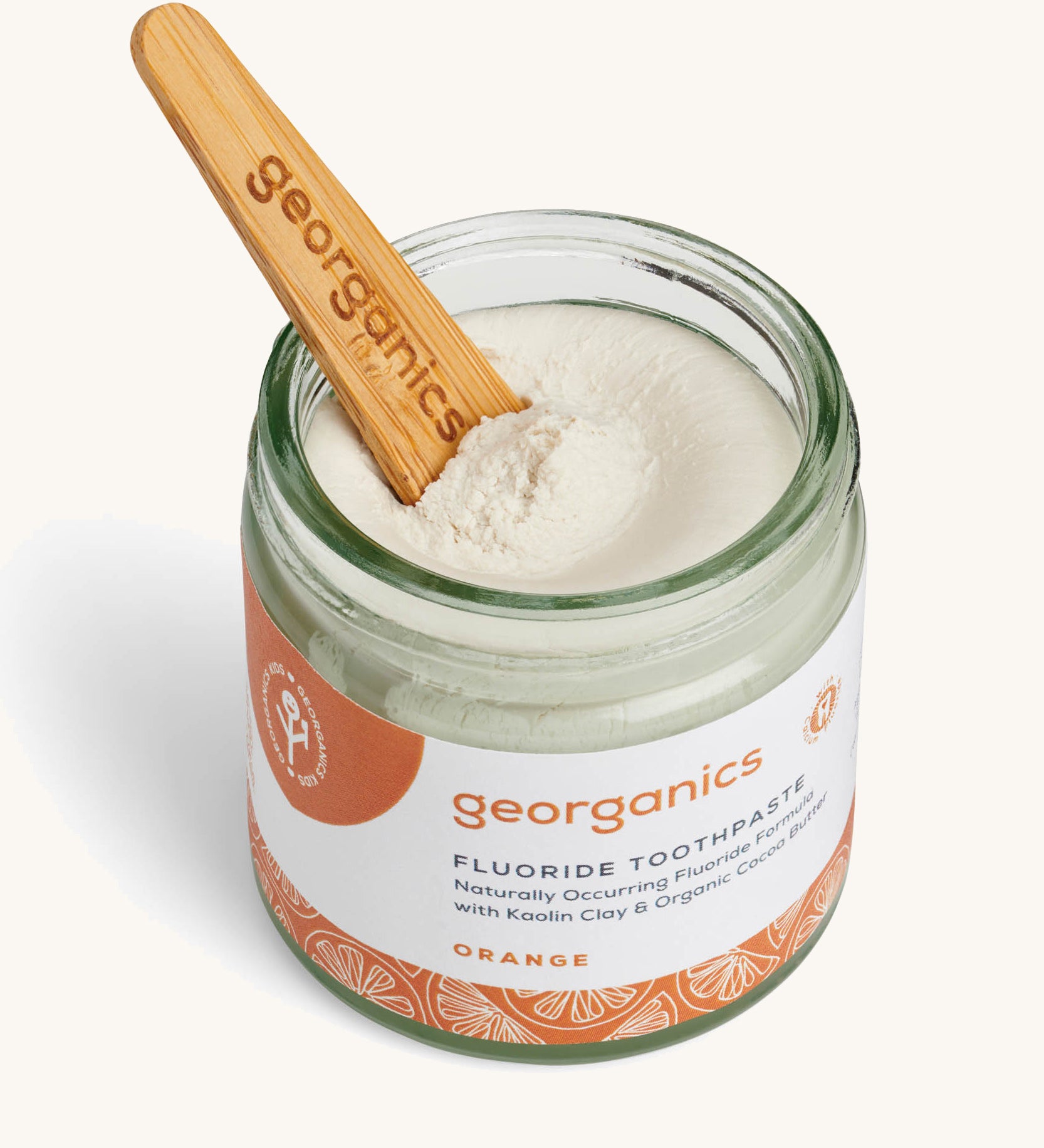 A opened jar of the orange fluoride toothpaste with the wooden spatula dipped in.