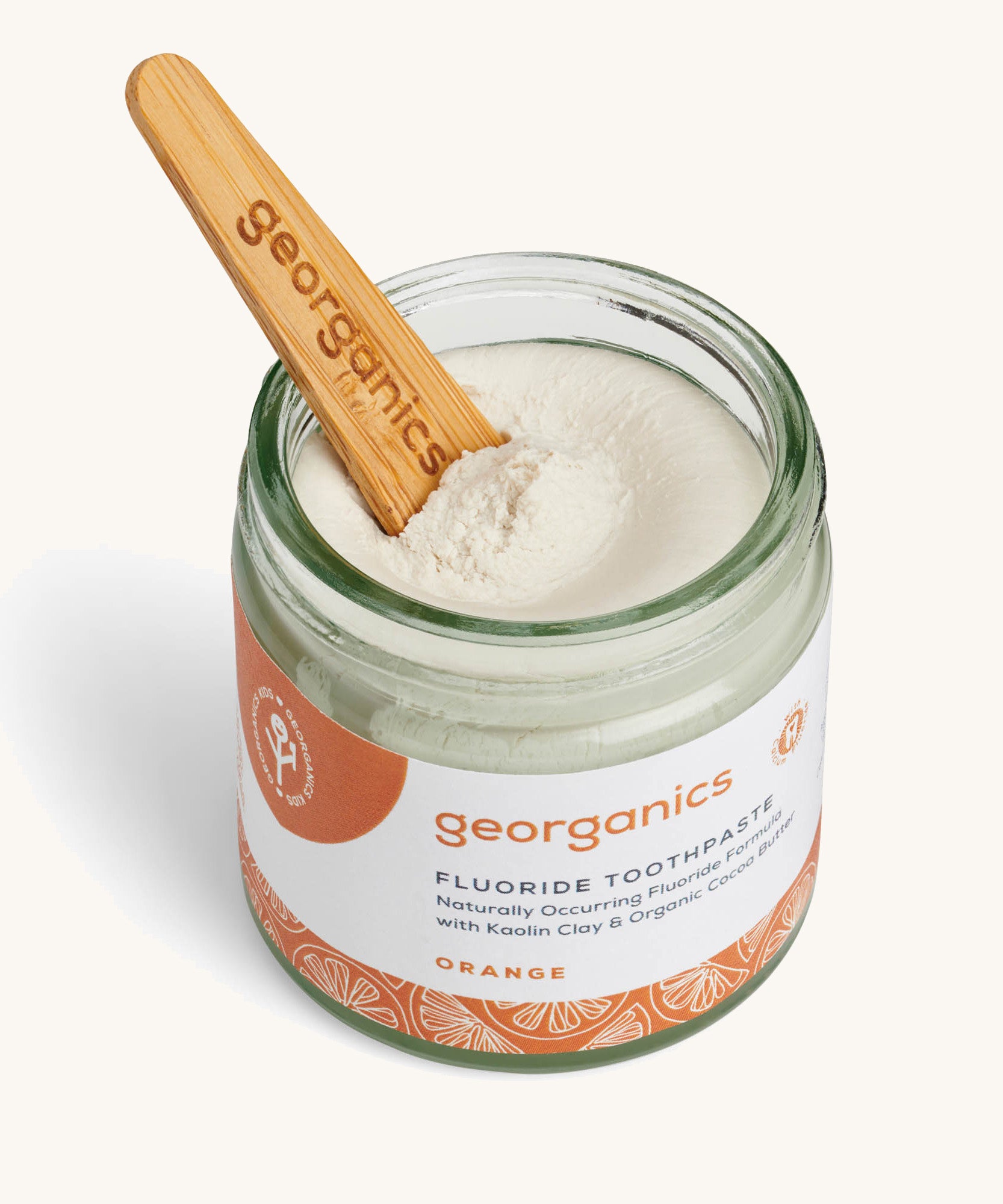 A opened jar of the orange fluoride toothpaste with the wooden spatula dipped in.