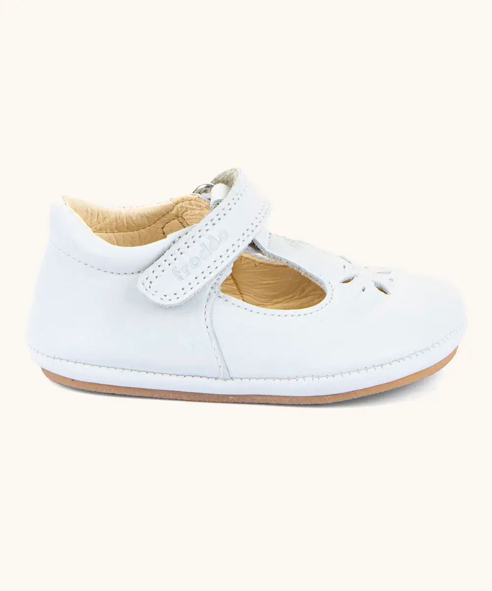 Side of Froddo barefoot pre walker baby shoe in white. A natural leather shoe with a velcro t bar strap and rubber sole