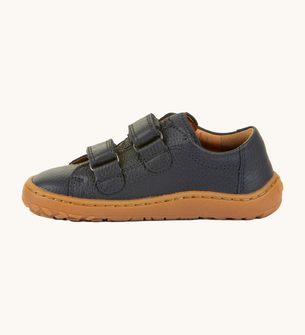 A side image of the Froddo barefoot base children's shoe in navy available at Babipur. A dark turquoise natural leather low profile shoe showing the 2 velcro fasteners looped through and the brown grippy sole