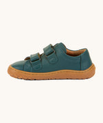 A side image of the Froddo barefoot base children's shoe in petroleum available at Babipur. A dark turquoise natural leather low profile shoe showing the 2 velcro fasteners looped through and the brown grippy sole