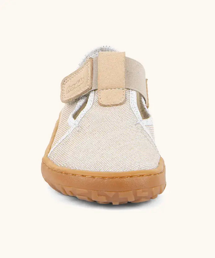 Front of Froddo barefoot canvas style kids shoes in pale cream with showing t-bar velcro fastener lopped through the eyelet 