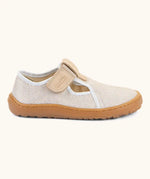 Side of Froddo barefoot canvas style kids shoes in pale cream  showing t-bar velcro fastener and brown rubber sole