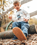 Child sitting on a log and wearing Froddo’s Barefoot Kids F-Motion TEX Shoes in dark blue showing close up of the flexible brown rubber sole tread