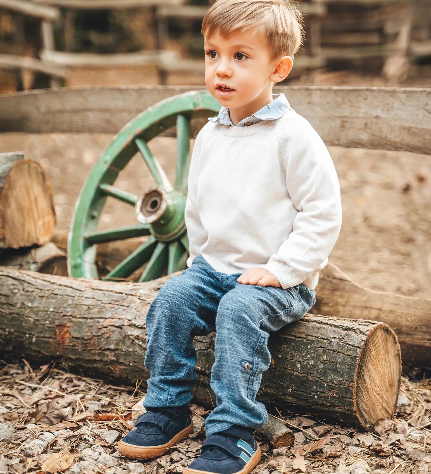 Child sitting on a log and wearing Froddo’s Barefoot Kids F-Motion TEX Shoes in dark blue