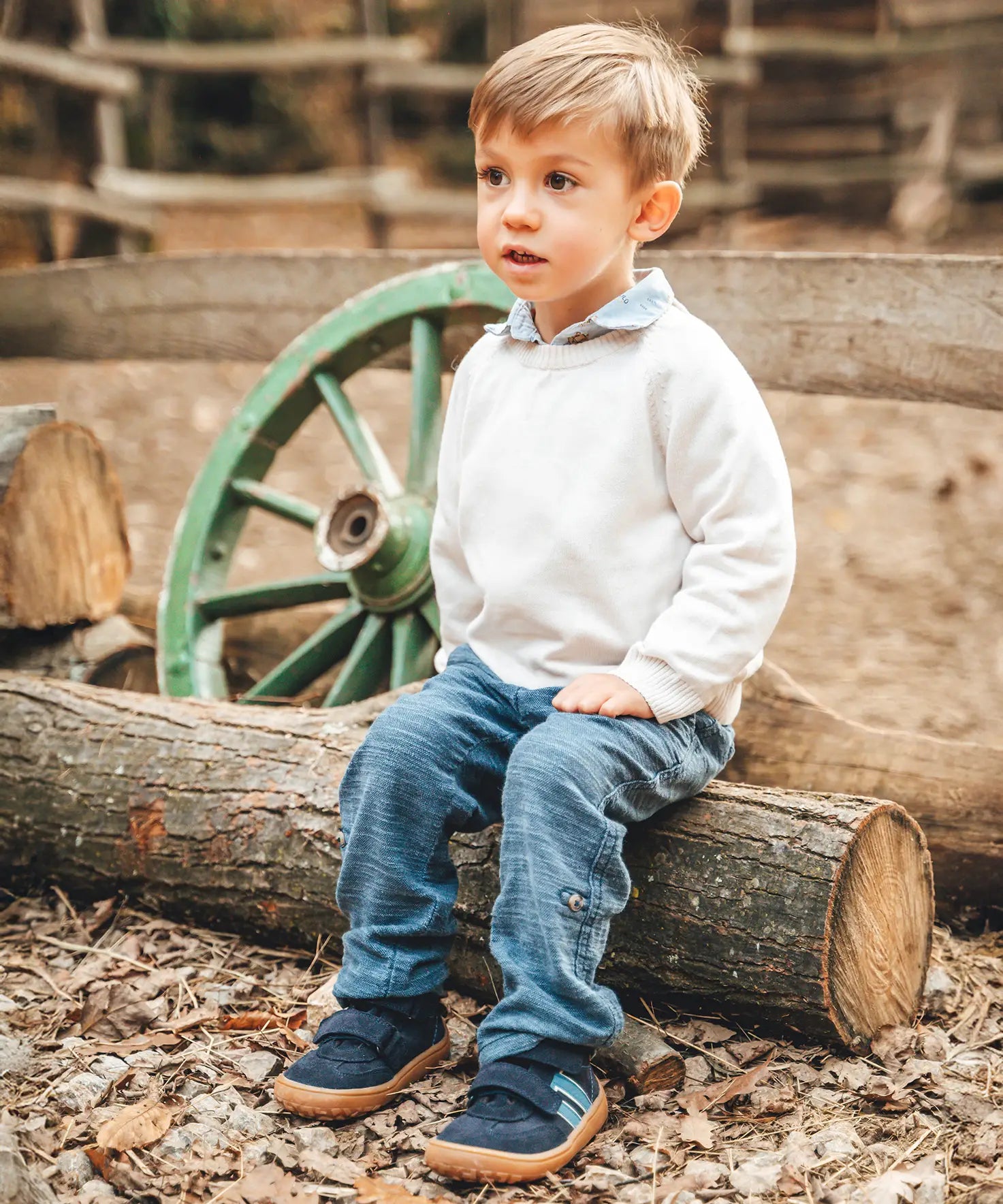 Child sitting on a log and wearing Froddo’s Barefoot Kids F-Motion TEX Shoes in dark blue