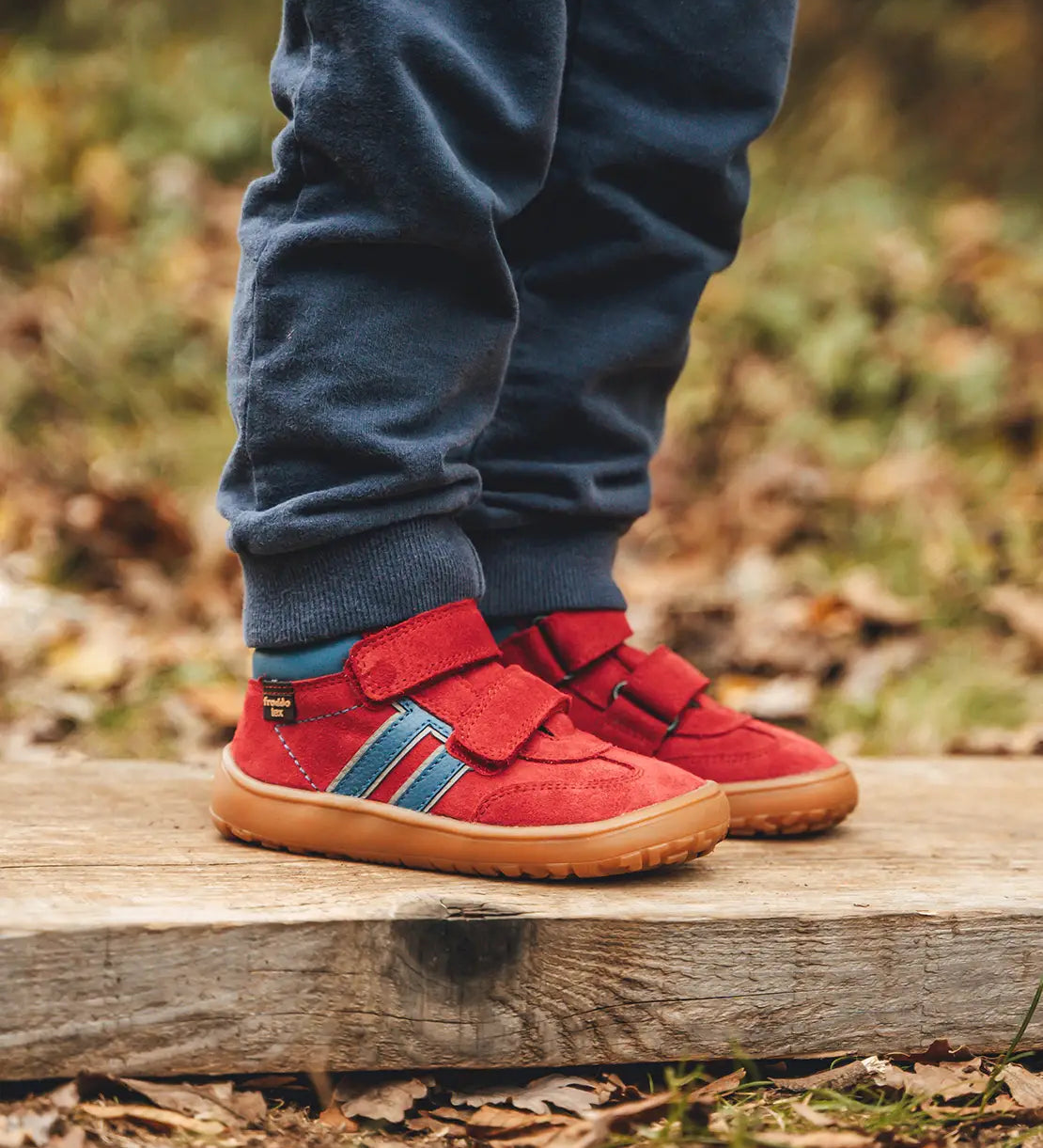 Child wearing Froddo’s Barefoot Kids F-Motion TEX Shoes in red outdoors showing the velcro fully fastened. Boot sits around the upper ankle