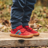 Child wearing Froddo’s Barefoot Kids F-Motion TEX Shoes in red outdoors showing the velcro fully fastened. Boot sits around the upper ankle