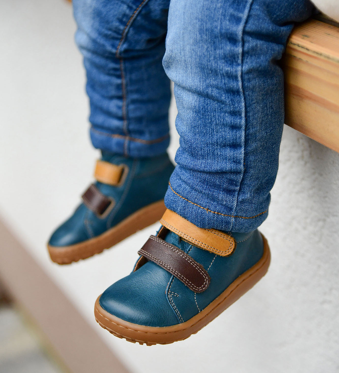 A child wearing the Froddo barefoot first step baby shoe in dark denim available at Babipur. A dark blue natural leather shoe with a 2 velcro fastener in dark yellow and brown for a secure fit. Features a light brown grippy sole
