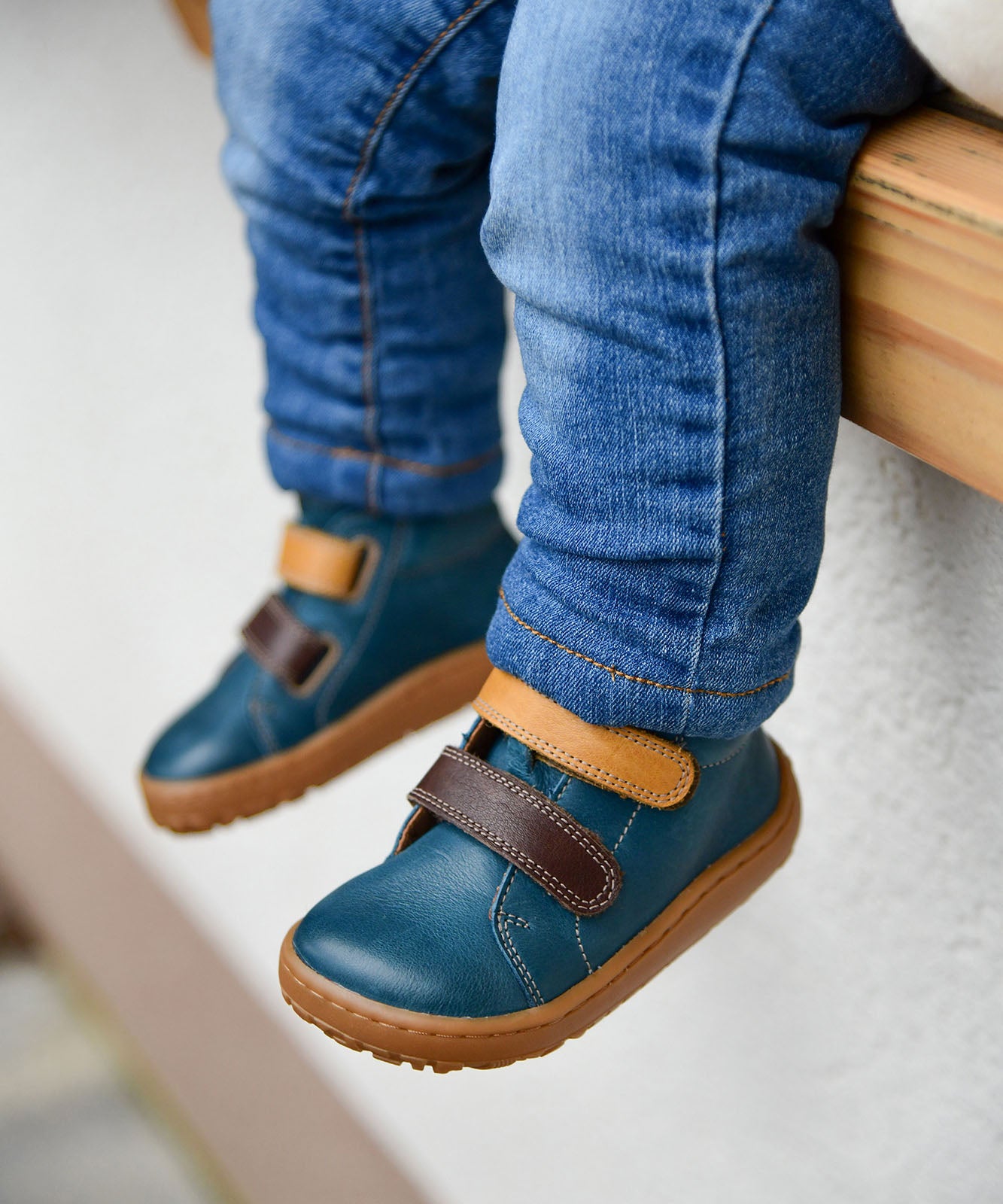 A child wearing the Froddo barefoot first step baby shoe in dark denim available at Babipur. A dark blue natural leather shoe with a 2 velcro fastener in dark yellow and brown for a secure fit. Features a light brown grippy sole