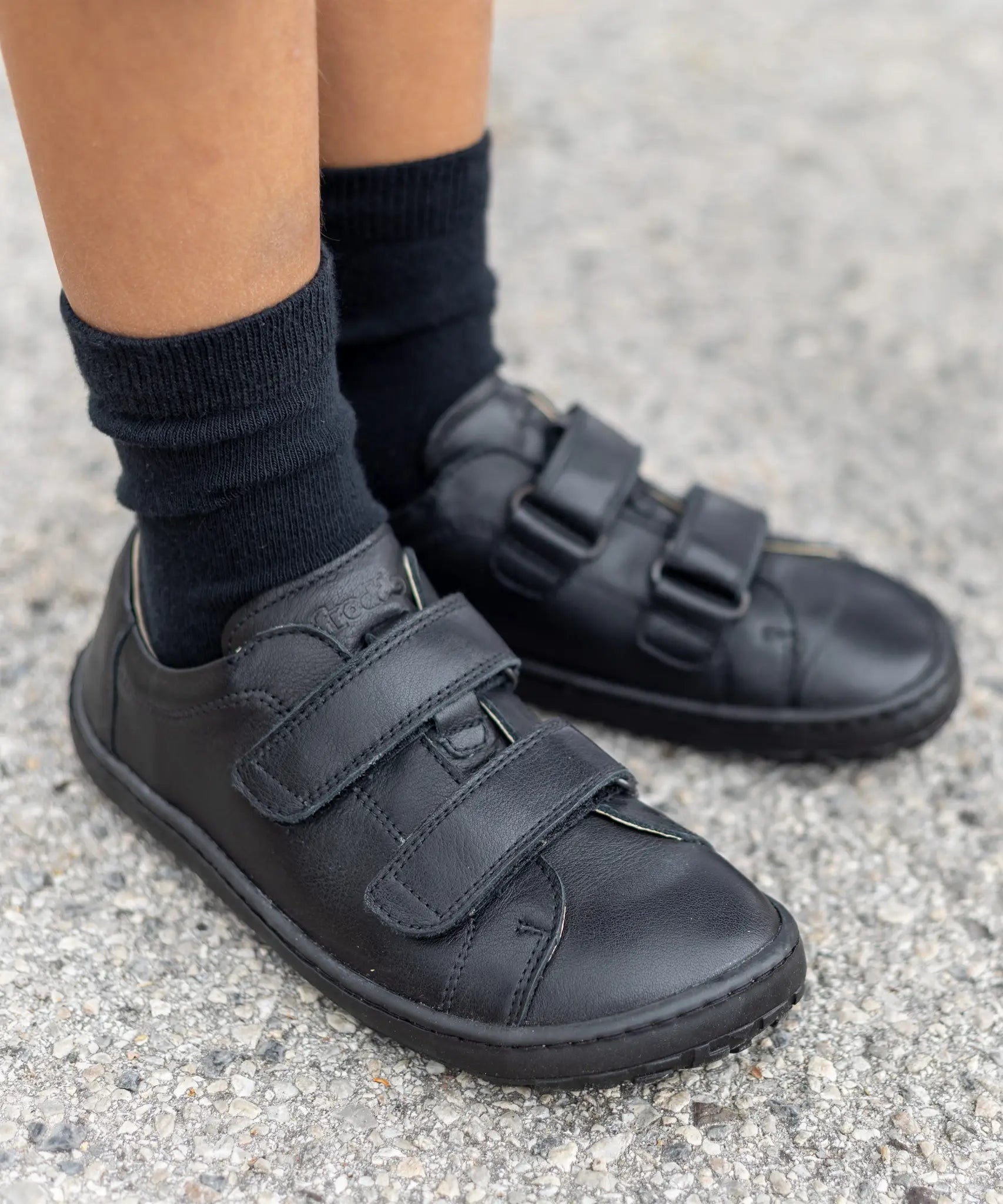 Child wearing Froddo's natural leather barefoot Alex school shoes in black showing 2 front velcro fasteners