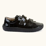 Side of Froddo barefoot kids school shoe in black patent. A low profile shoe with 2 front velcro straps with a decoration on the end