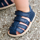 Small child wearing Froddo's barefoot natural leather sandal in dark blue standing on a concrete surface