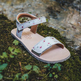 A Froddo's barefoot kids natural leather Lia sandal in pink with flowers standing on green moss