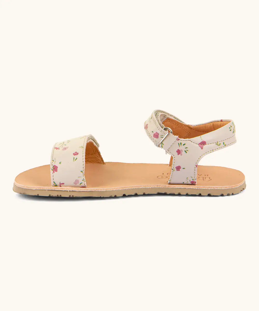Side of Froddo barefoot kids natural leather sandal in pink with flowers. Showing strap looped through the eyelet on the ankle