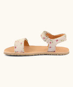 Side of Froddo barefoot kids natural leather sandal in pink with flowers. Showing strap looped through the eyelet on the ankle