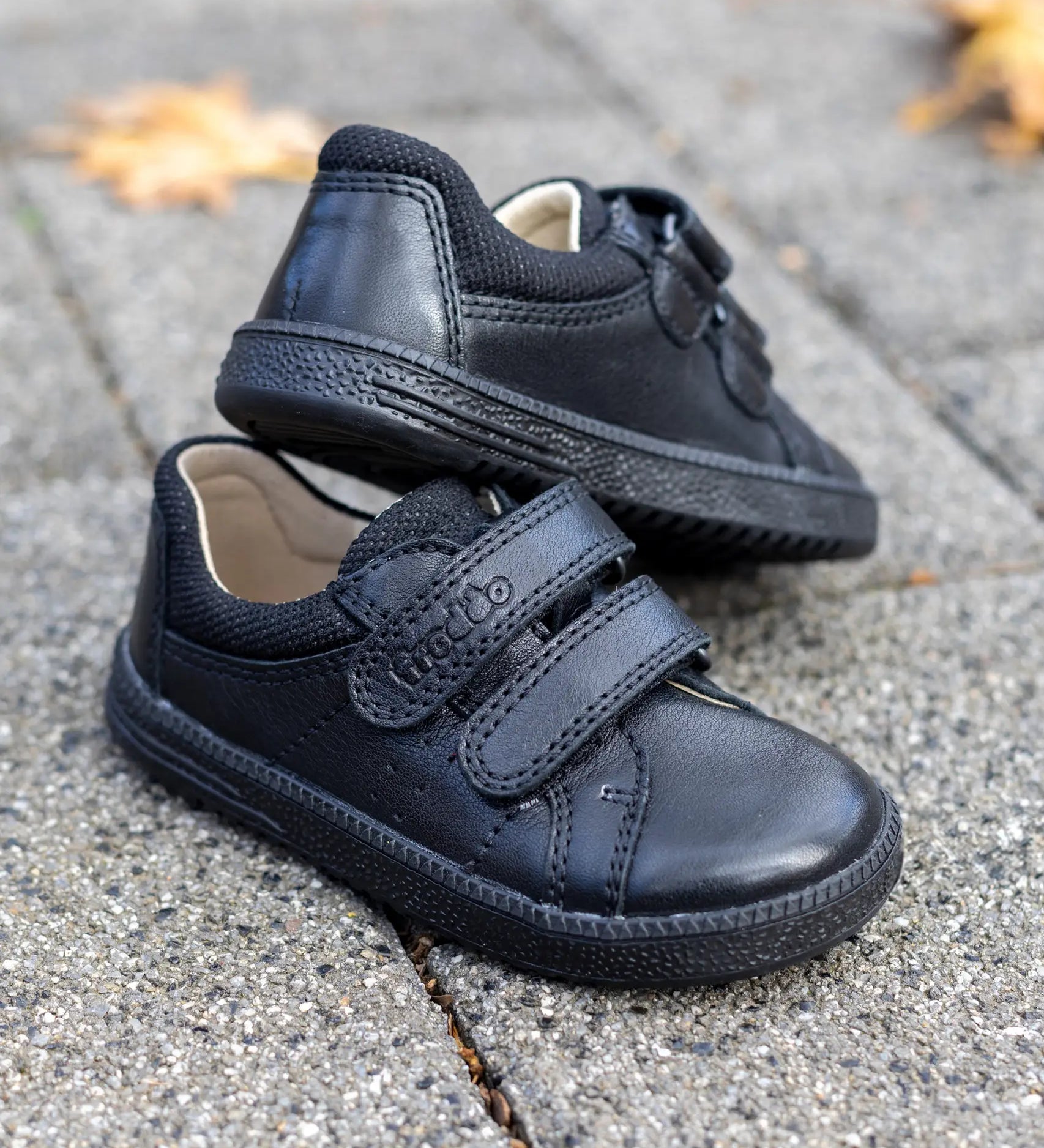 Pair of Froddo barefoot natural leather kids Steve school shoes in black standing on a concrete surface