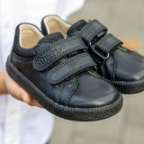 Child hands holding a pair of Froddo barefoot natural leather kids Steve school shoes in black 