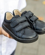 Child hands holding a pair of Froddo barefoot natural leather kids Steve school shoes in black 