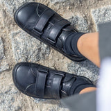 Child wearing Froddo's natural black leather barefoot school shoes showing the 2 front velcro fasteners