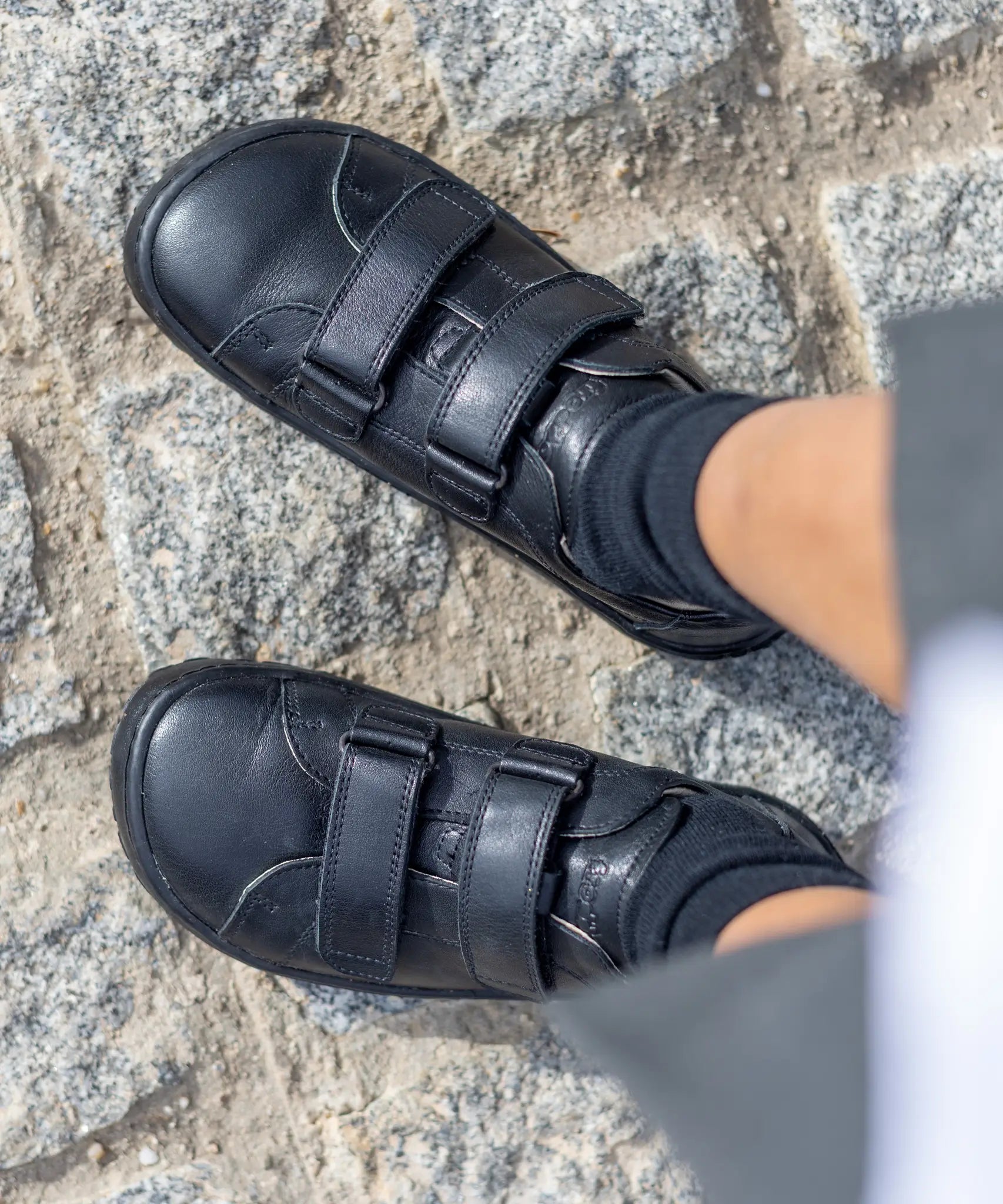 Child wearing Froddo's natural black leather barefoot school shoes showing the 2 front velcro fasteners