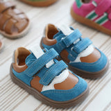 Froddo barefoot zeru Spring kids shoes in blue brown and white standing on a beige striped floor next to other trainers and sandals