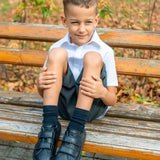 Child sitting on a wooden bench wearing Froddo's natural black leather barefoot school shoes showing front velcro fasteners