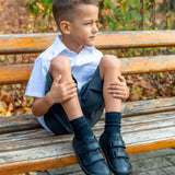 Child wearing Froddo's natural black leather barefoot school shoes and sitting on a wooden bench