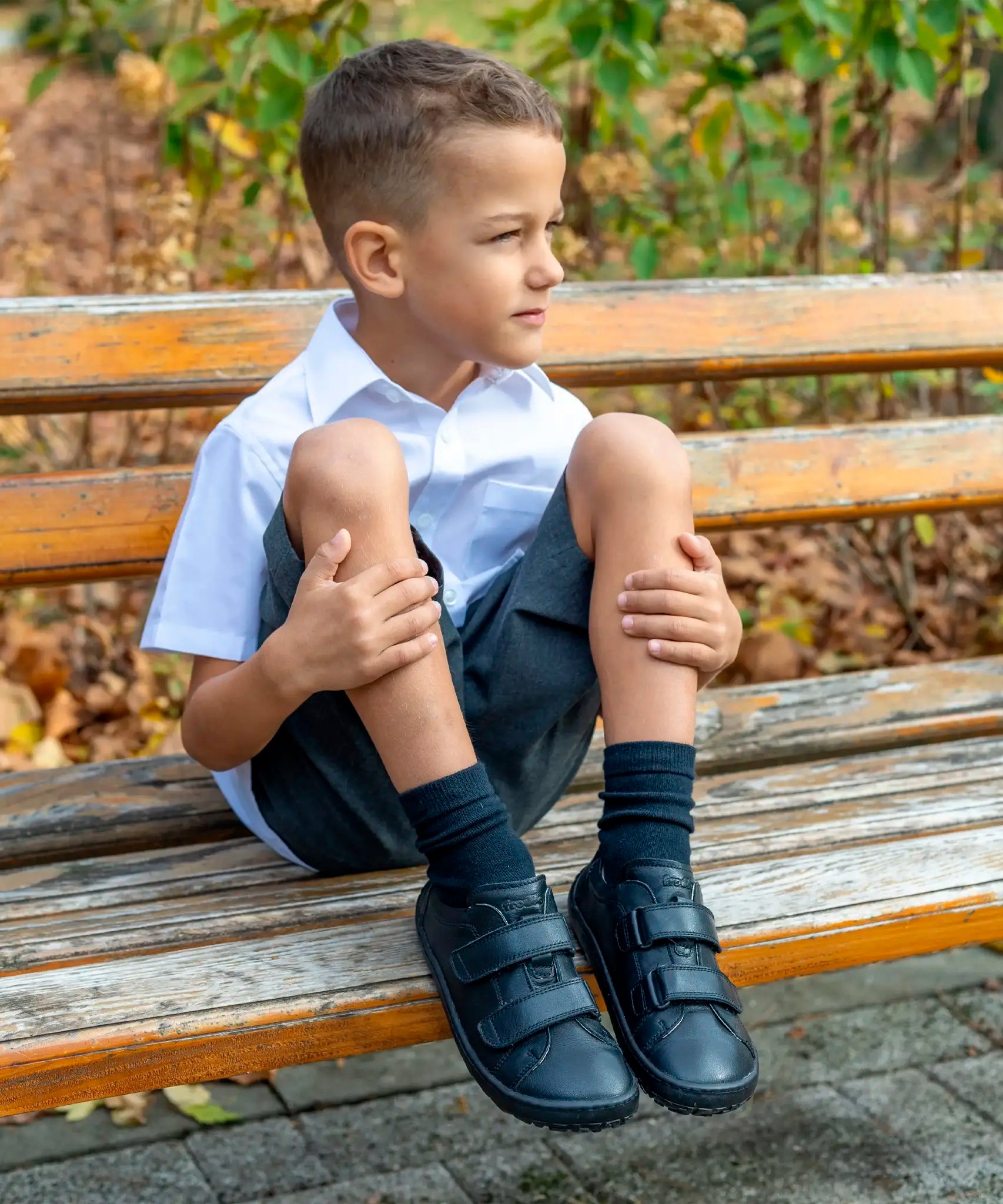 Child wearing Froddo's natural black leather barefoot school shoes and sitting on a wooden bench