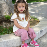 Small child wearing Froddo's barefoot zeru Spring kids shoes in light and dark pink. Sitting on a stone surface with trees and plants in the background