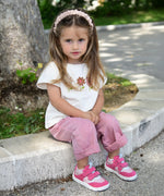 Small child wearing Froddo's barefoot zeru Spring kids shoes in light and dark pink. Sitting on a stone surface with trees and plants in the background