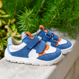 Pair of Froddo barefoot zeru Spring kids shoes in blue and white on a stone surface with plants in the background