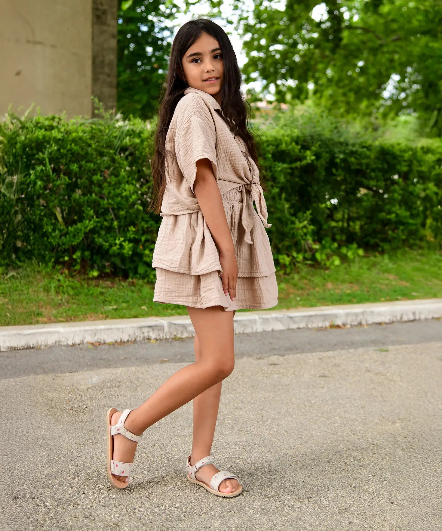 Child wearing Froddo's barefoot kids natural leather lia sandals in pink with flowers on a concrete surface outdoors