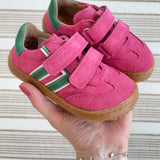 Adult holding Froddo's barefoot f-motion kids trainers in bright pink with green stripe design showing brand name on velcro strap