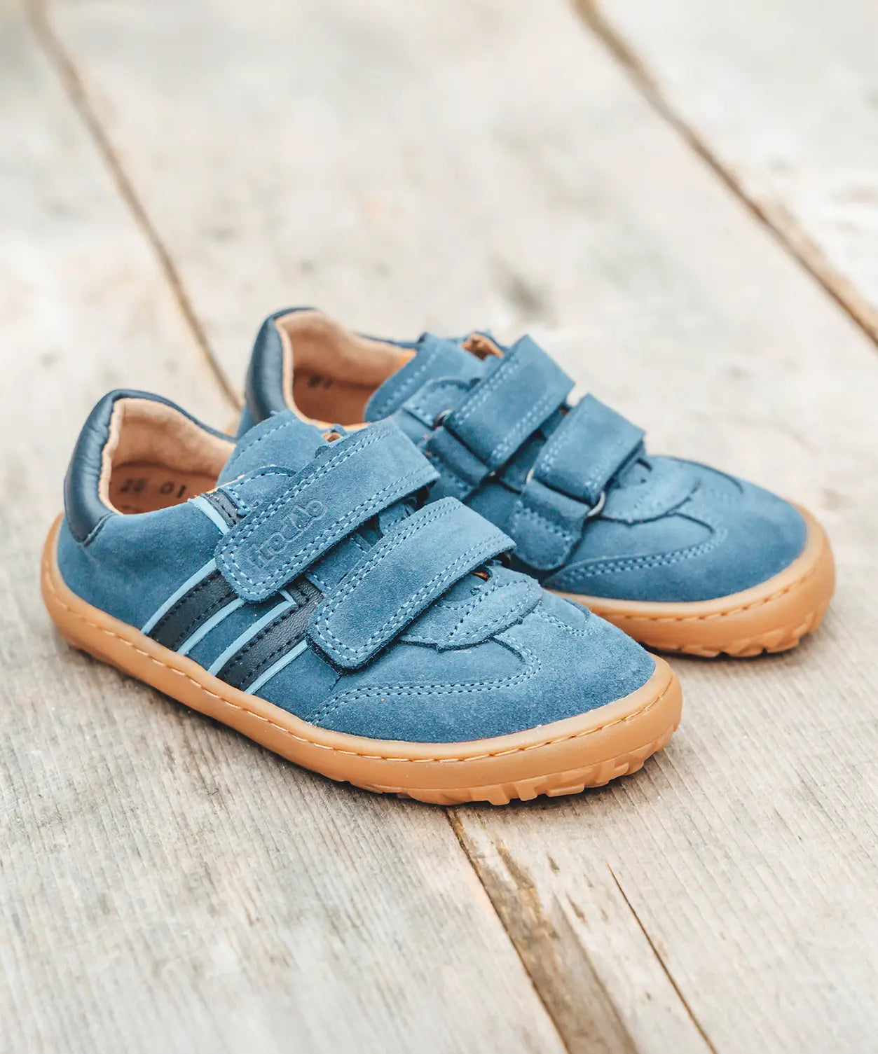 Pair of Froddo barefoot f-motion kids suede shoes in denim blue on decking. Sports trainer has a wide, foot shaped toe box and zero heel drop