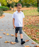 Child wearing Froddo's natural leather barefoot Alex school shoes in black and walking on a concrete path in a park