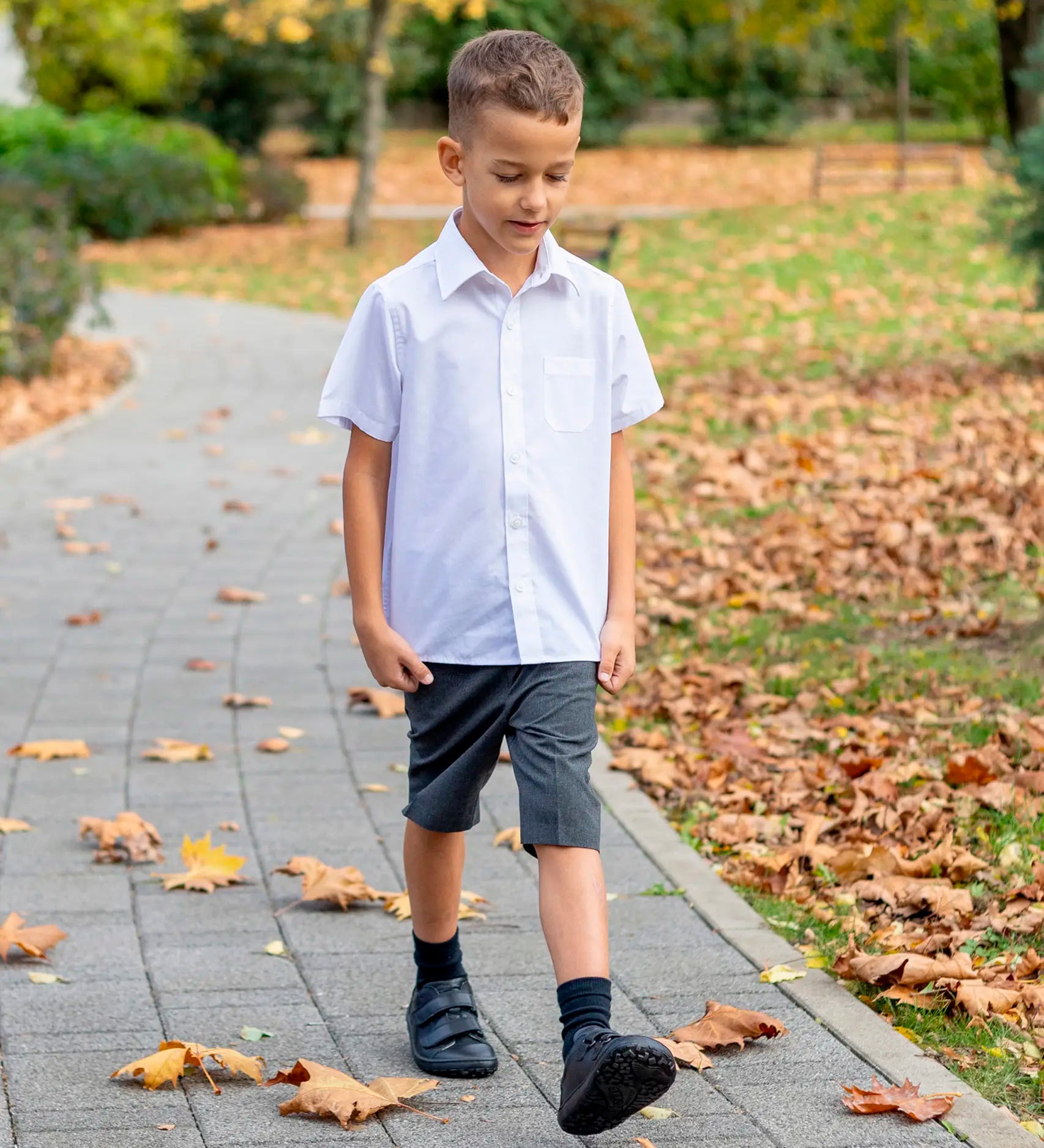 Child wearing Froddo's natural leather barefoot Alex school shoes in black and walking on a concrete path in a park