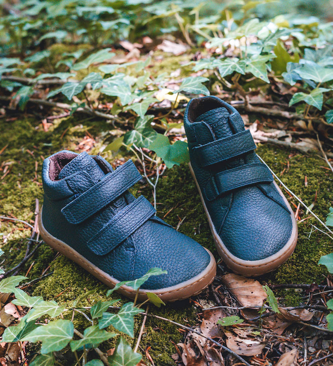 Froddo barefoot Autumn children's shoe in navy standing on a leaves. A natural leather shoe with a 2 velcro fastener for a secure fit, padded ankle and a dark brown grippy sole available at Babipur.