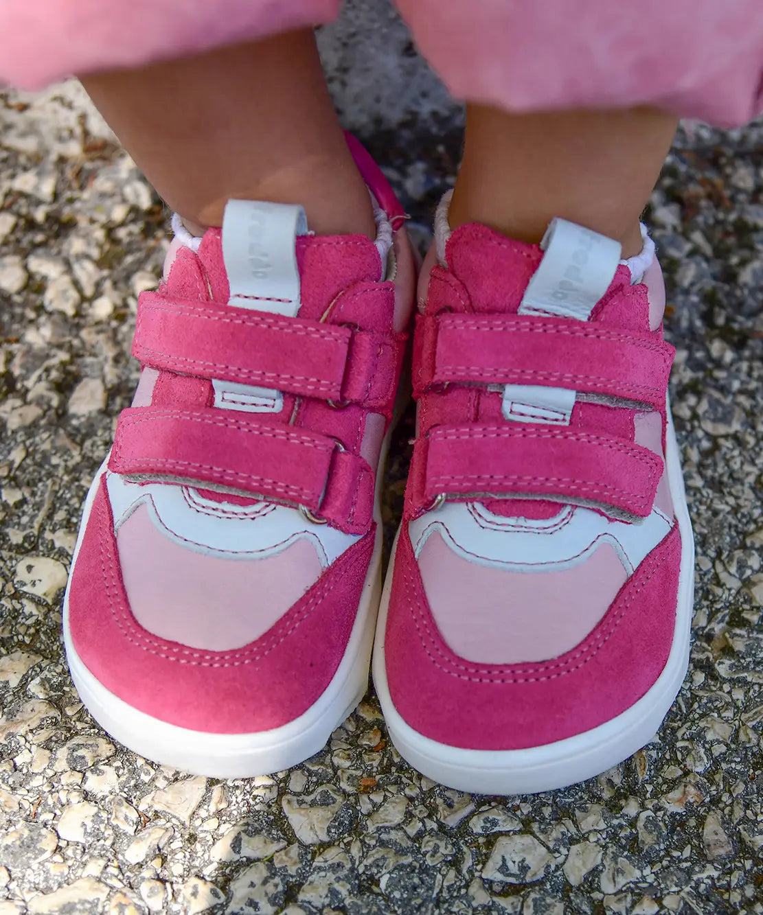 Small child wearing Froddo's barefoot zeru Spring kids shoes in light and dark pink showing front velcro straps fastened