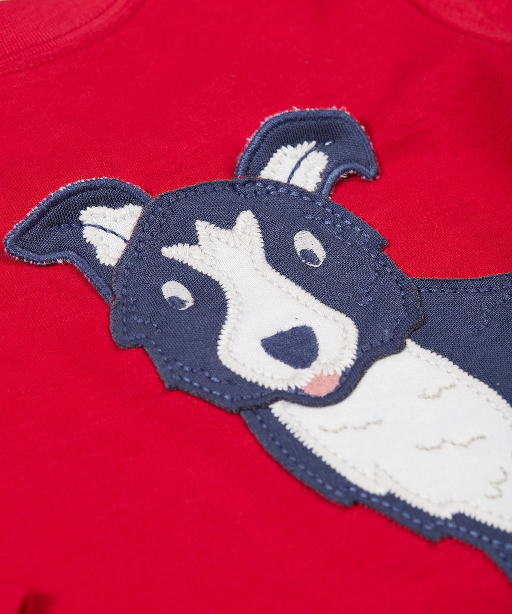 A close up of the Frugi kids adventure applique top berry red/sheepdog top showing the sheepdog applique detail on red organic cotton fabric.