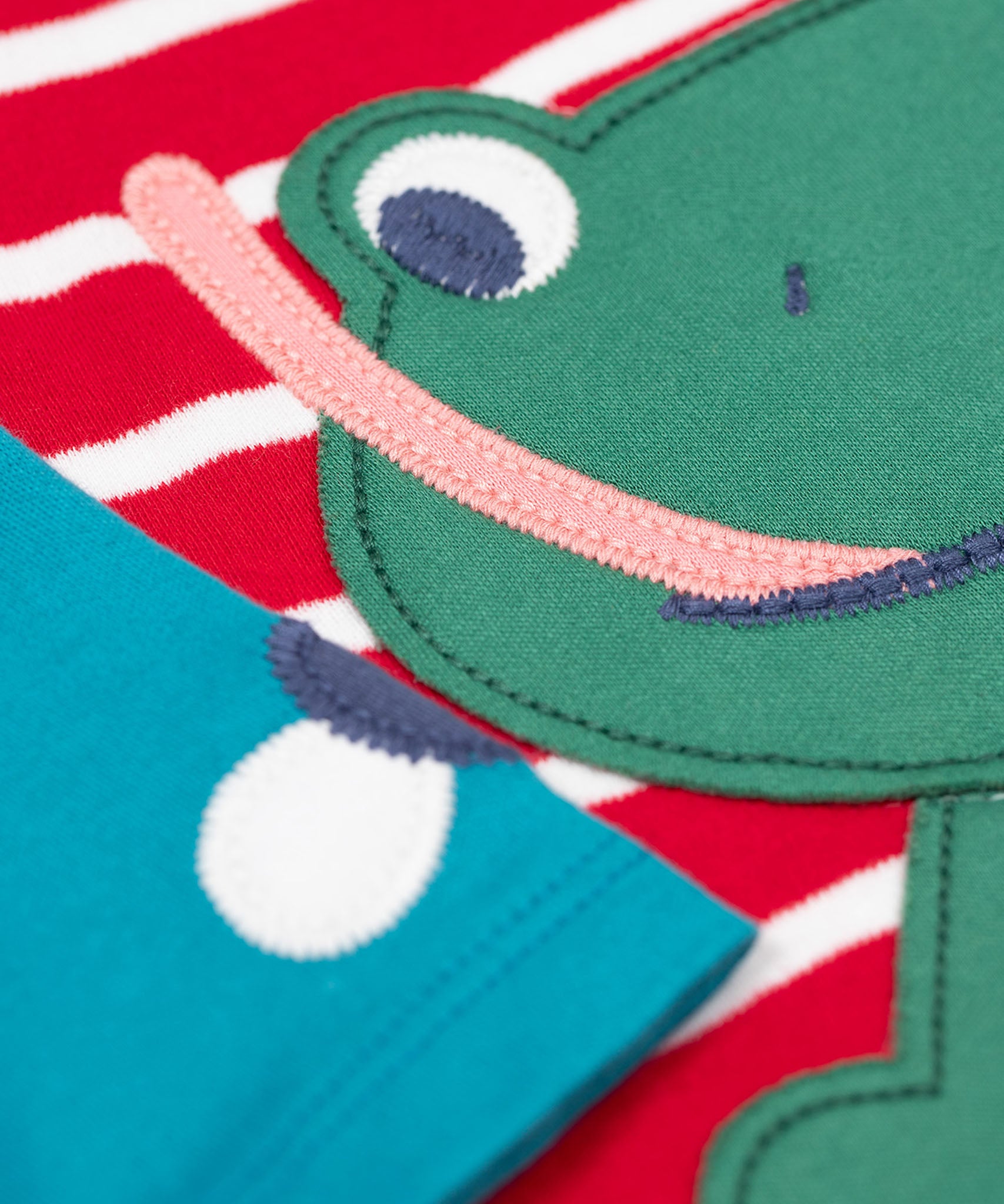 A close up of the Frugi kids alfie raglan berry red breton frog top showing the playful green frog applique detial on organic cotton fabric.